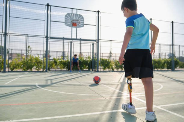 Two friends playing football, one of them has a leg prosthesis and is kicking a penalty. Kids playing sports together.